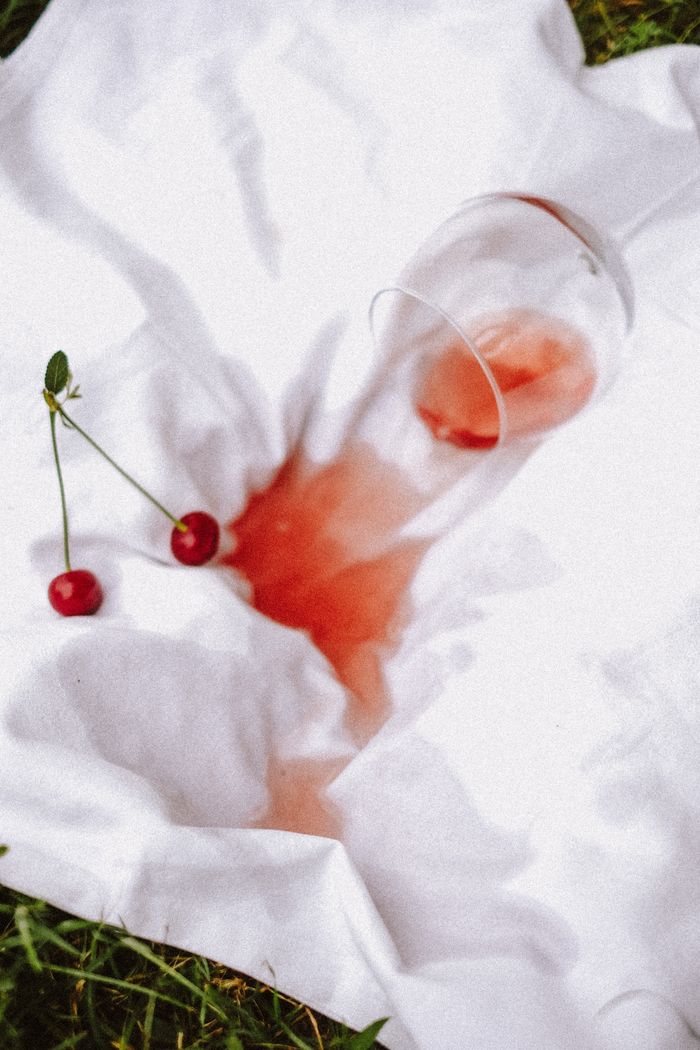 A creative shot of spilled cherry juice with cherries on white sheet.
